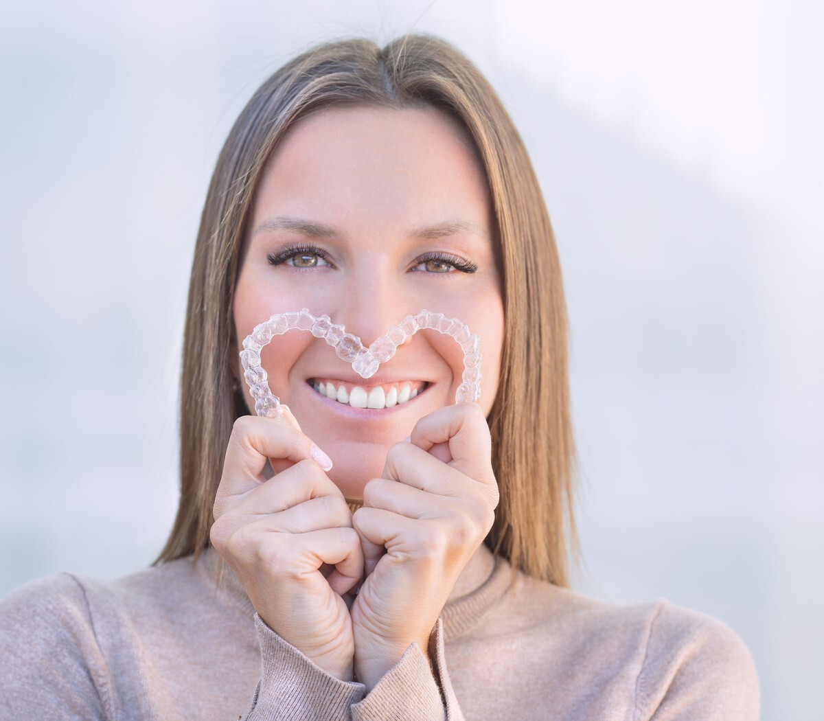 Woman smiling while holding two clear aligners in a heart shape
