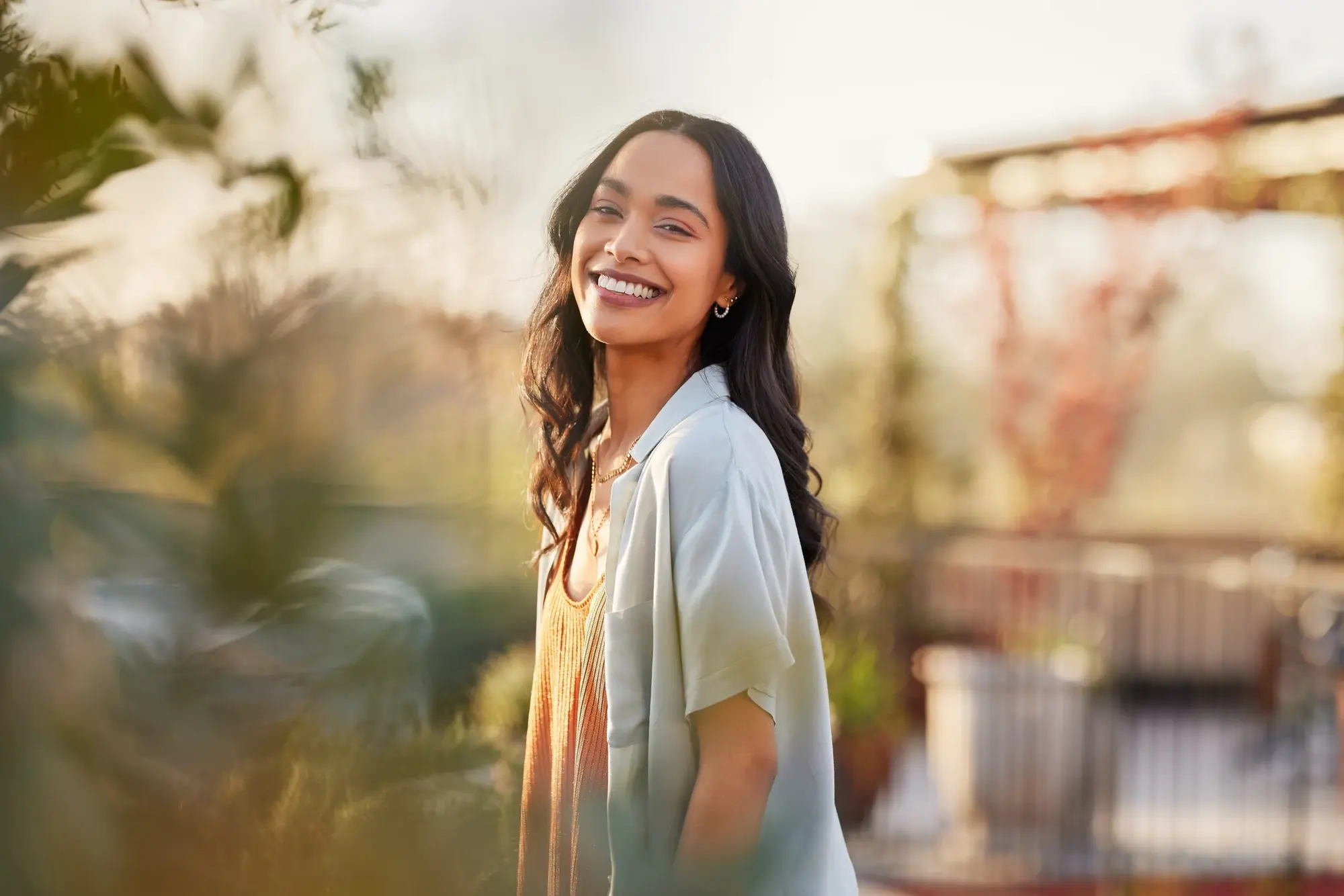Woman with long dark hair smiling outdoors in warm sunlight